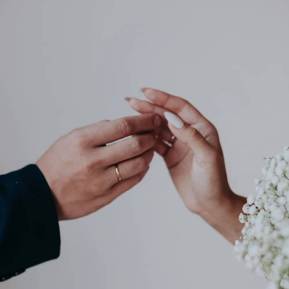 Manos entrelazadas de la pareja junto a un ramo de flores blancas