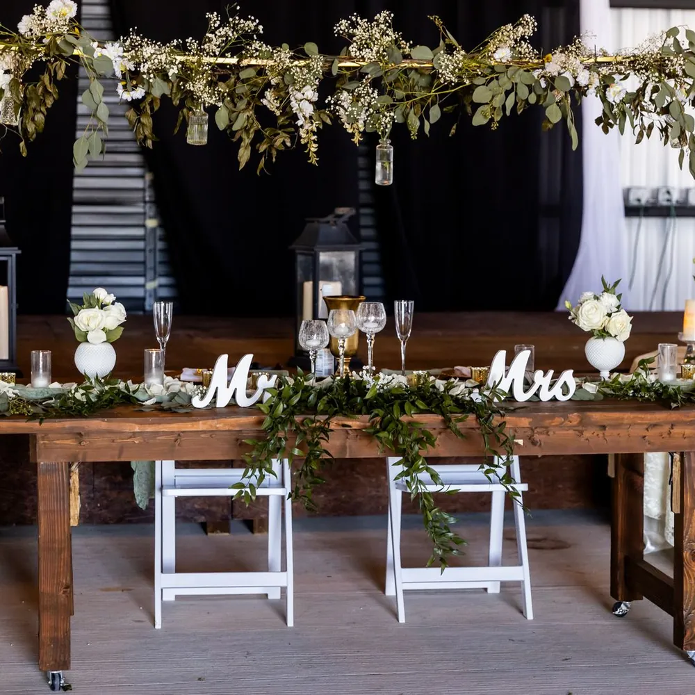 Mesa de novios decorada con follaje verde, velas y las palabras Mr y Mrs