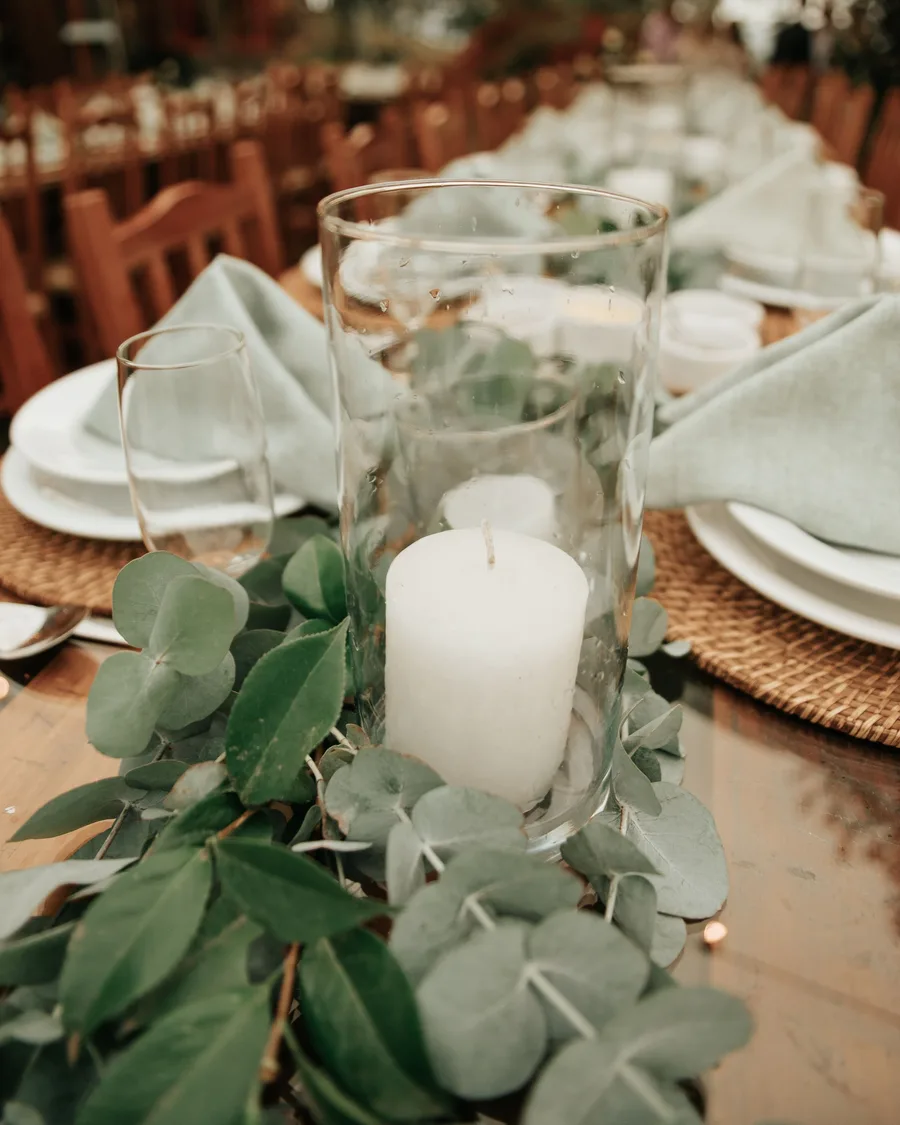 Mesa de banquete con velas, follaje verde y vajilla elegante