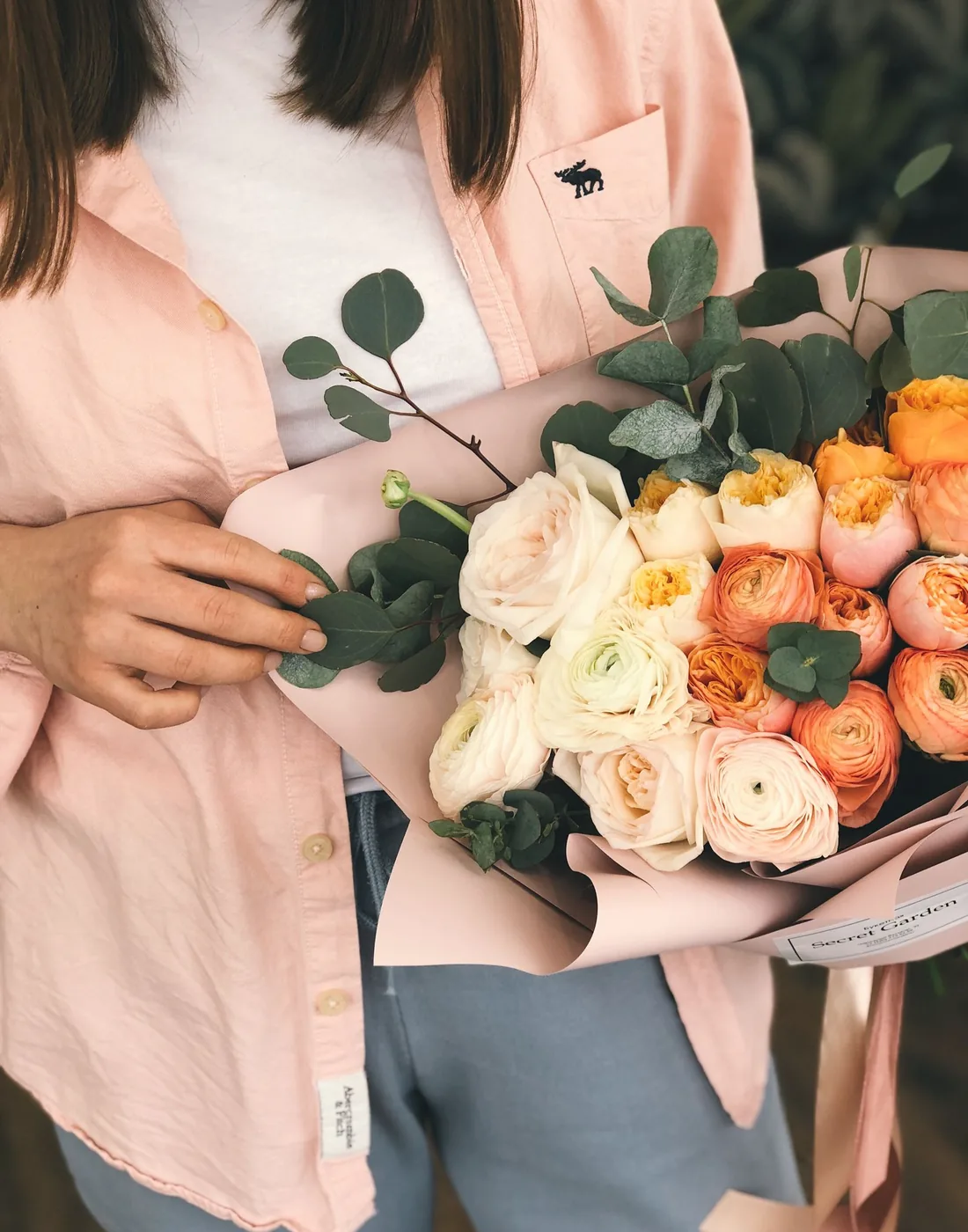 Detalle de un ramo de rosas y ranúnculos en tonos durazno y crema, sostenido con cariño