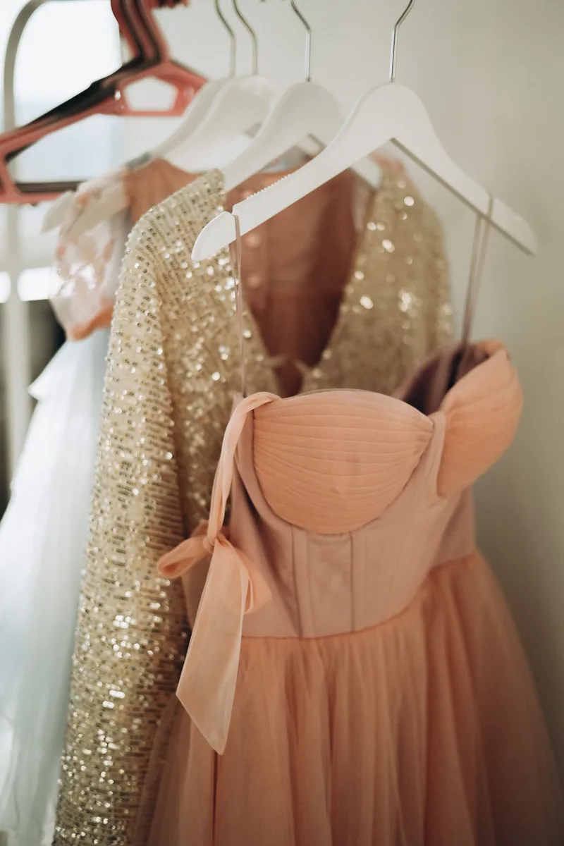 Vestidos largos de gala en tonos durazno y lentejuela, colgados en sus ganchos