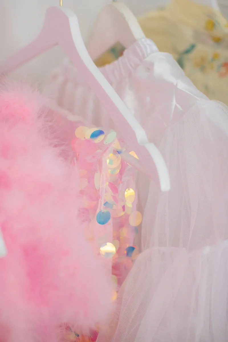 Vestidos de gala con lentejuela y tul rosa, colgados en ganchos blancos
