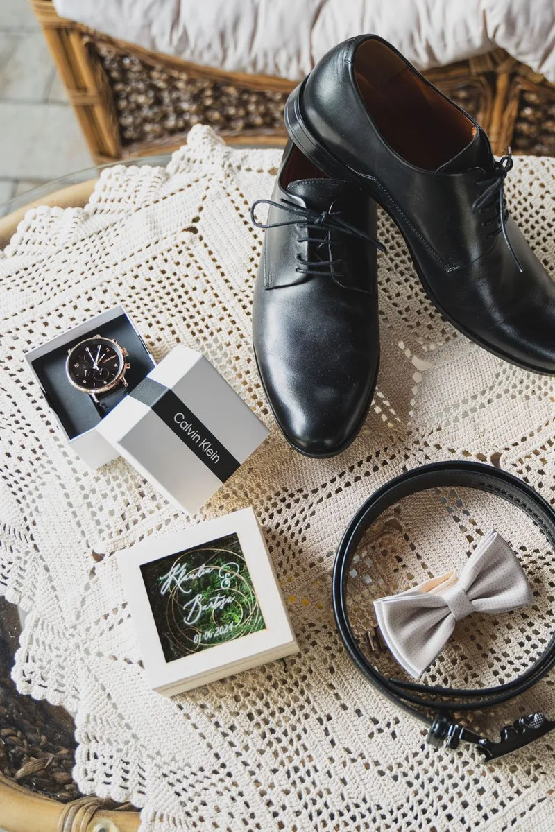 Zapatos de vestir, reloj, moño y frasco de perfume sobre un mantel de encaje